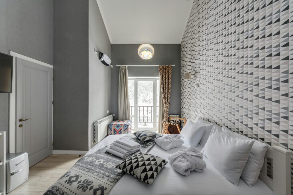 Stylish bedroom featuring geometric wallpaper, cozy bed, and natural light.